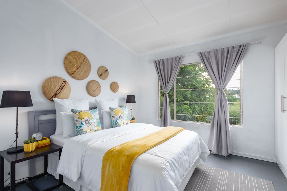 A bedroom with a bed, nightstands, a window with curtains, and decorative wall hangings.