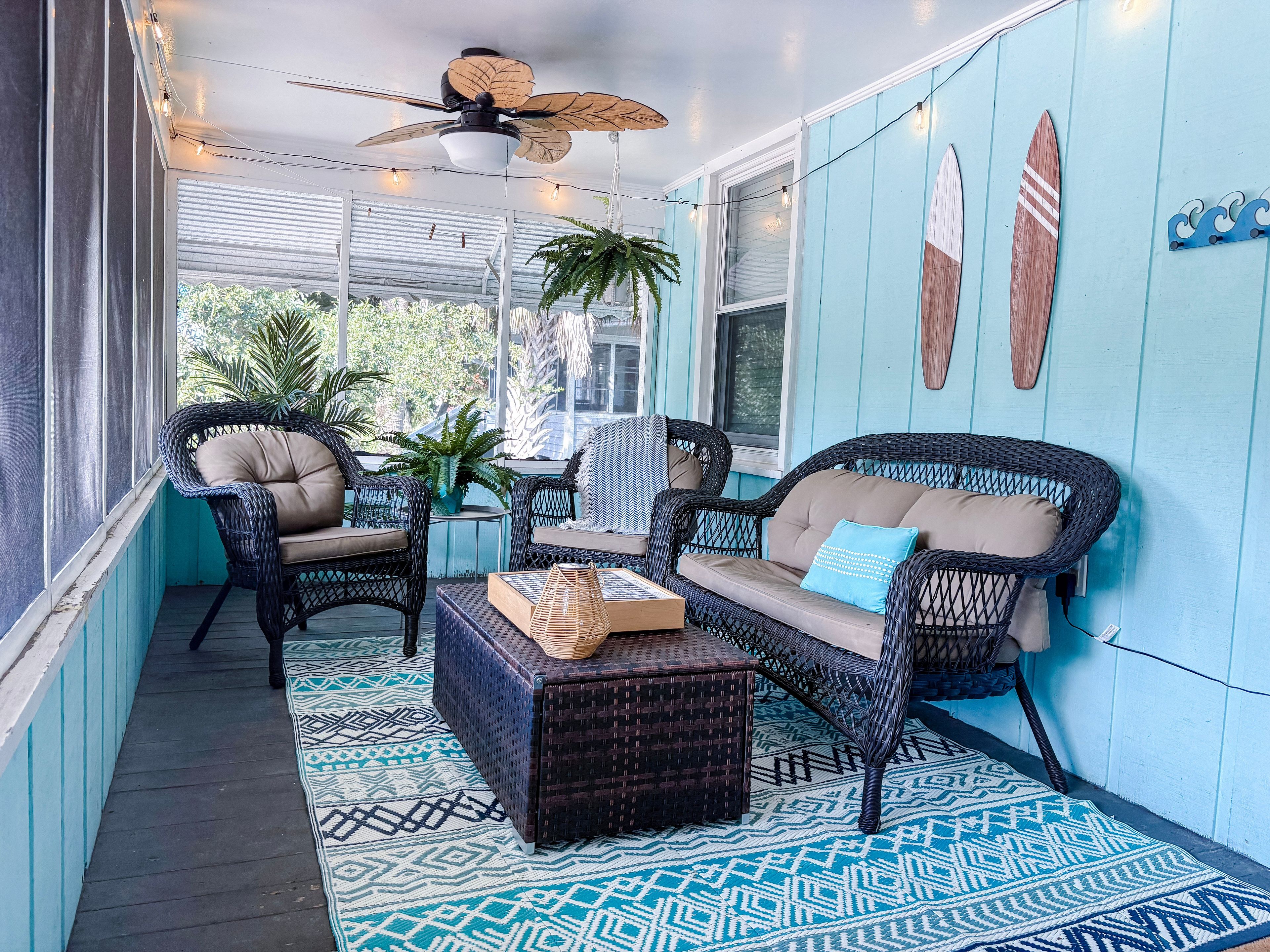 A covered porch with wicker furniture, a ceiling fan, string lights, and a view of the outdoors.