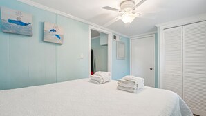 Ein Schlafzimmer mit einem Bett, zwei an der Wand befestigten Kunstwerken, einem Deckenventilator, einem Schrank und einer Tür zu einem anderen Raum.
