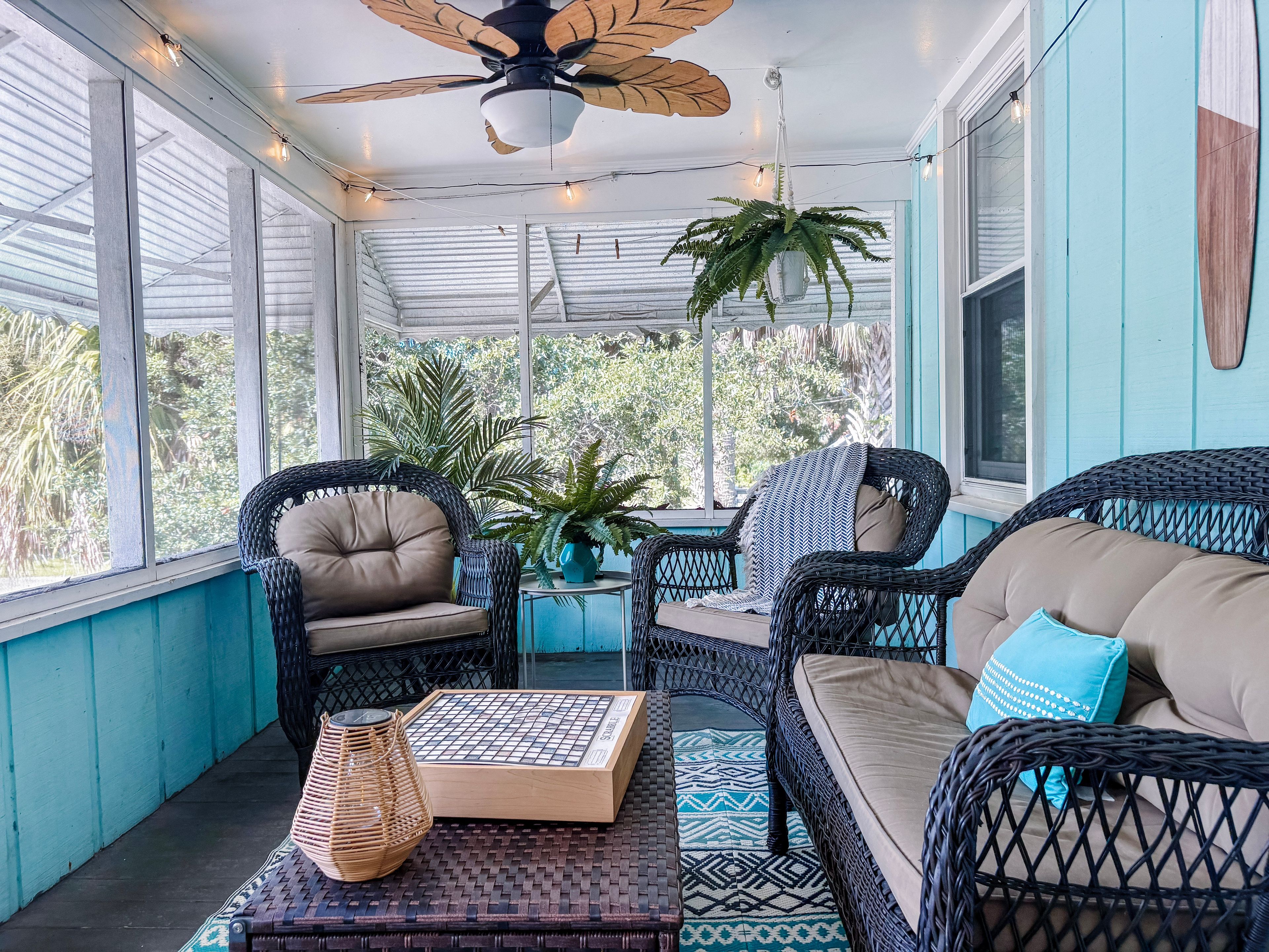 A sunroom with wicker furniture, a ceiling fan, and a view of greenery outside.