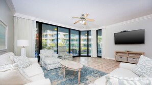 Ein modernes Wohnzimmer mit einem großen Flachbildfernseher, einem Deckenventilator und Blick auf einen Balkon mit Pool.