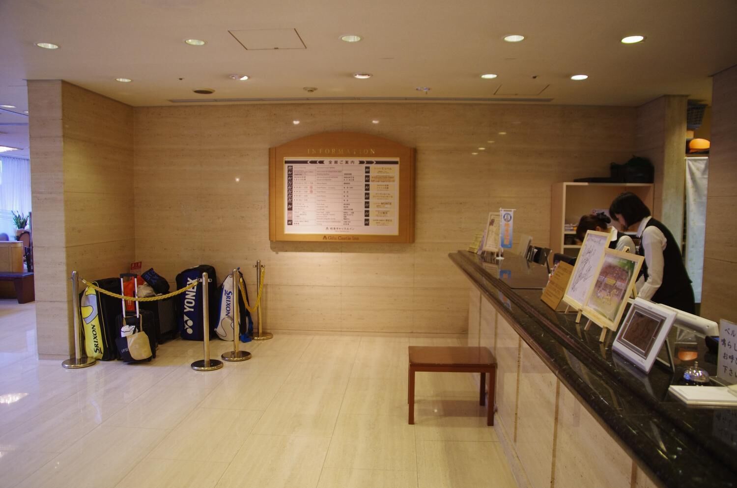 Een hotel receptie met een houten balie, een prikbord met informatie en bagageruimte met gele touwen.