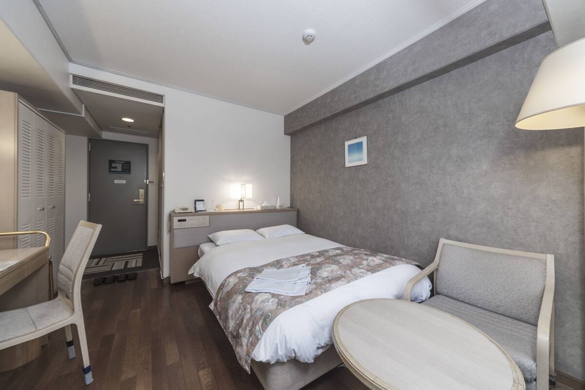 A hotel room with a bed, bedside table, chair, and a small table.