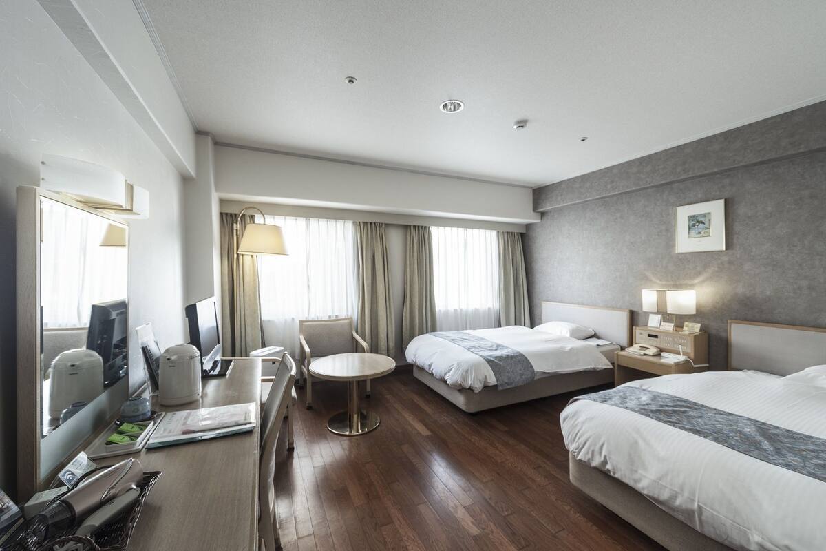 A hotel room with two beds, a desk with a chair, a small round table, and a mirror.