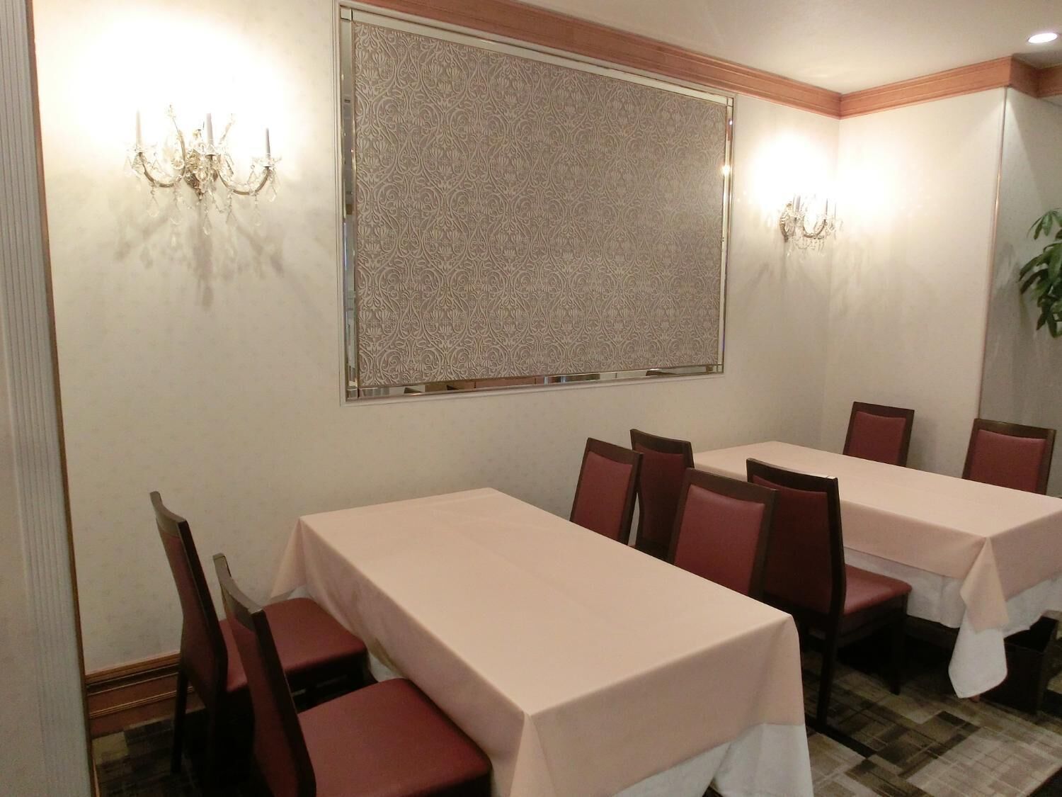 A conference room with two long tables, red chairs, patterned wallpaper, and wall sconces.