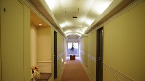Un couloir d’hôtel avec un sol recouvert de moquette, des portes doubles de chaque côté et une fenêtre au bout.
