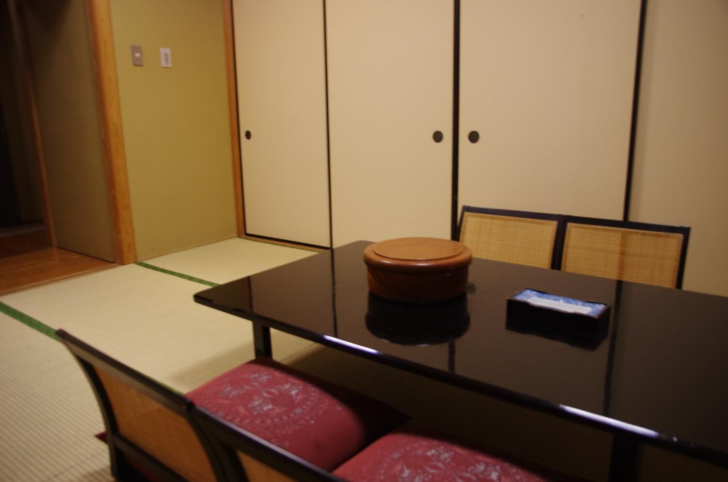 A traditional Japanese room with tatami mat flooring, a low table with a wooden stool, and shoji screens in the background.