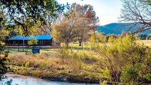 A rustic cabin with a blue roof, surrounded by a grassy field and a small stream. - Panoramic Country Views ~ Wildlife ~ Butterflies & Birds ~ Star-gazing ~ Hiking (Leakey)