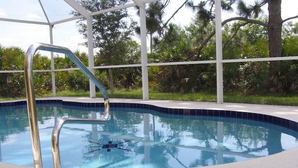 A swimming pool with a metal ladder, surrounded by a white fence and lush greenery. - 3 Bedroom Home with Heated Private Pool Close to Golf & Beach (Rotonda lakes)