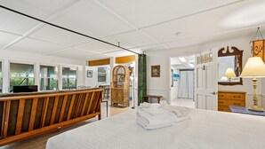 Un'ampia camera da letto con un letto grande, una panca in legno, una poltrona in vimini e vista sull'esterno attraverso ampie finestre.