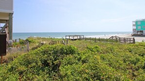 Vista sulla spiaggia con una struttura in legno, una recinzione e un edificio sullo sfondo.