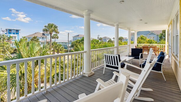Eine überdachte Veranda mit weißen Geländern, einer Holzterrasse und Gartenmöbeln.