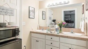 A bathroom with two sinks, a mirror, a microwave, and a sign on the door.