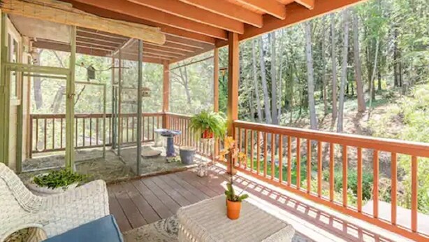 A covered outdoor area with wooden flooring, a railing, and a view of a forest.