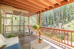 Un espacio al aire libre techado con piso de madera, barandilla y vista a un bosque.