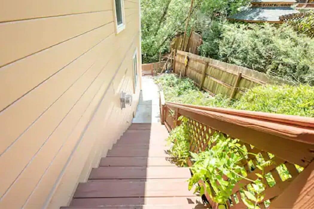 Un escalier étroit en bois mène à une terrasse dotée d’une rambarde en bois et de plantes en pot.