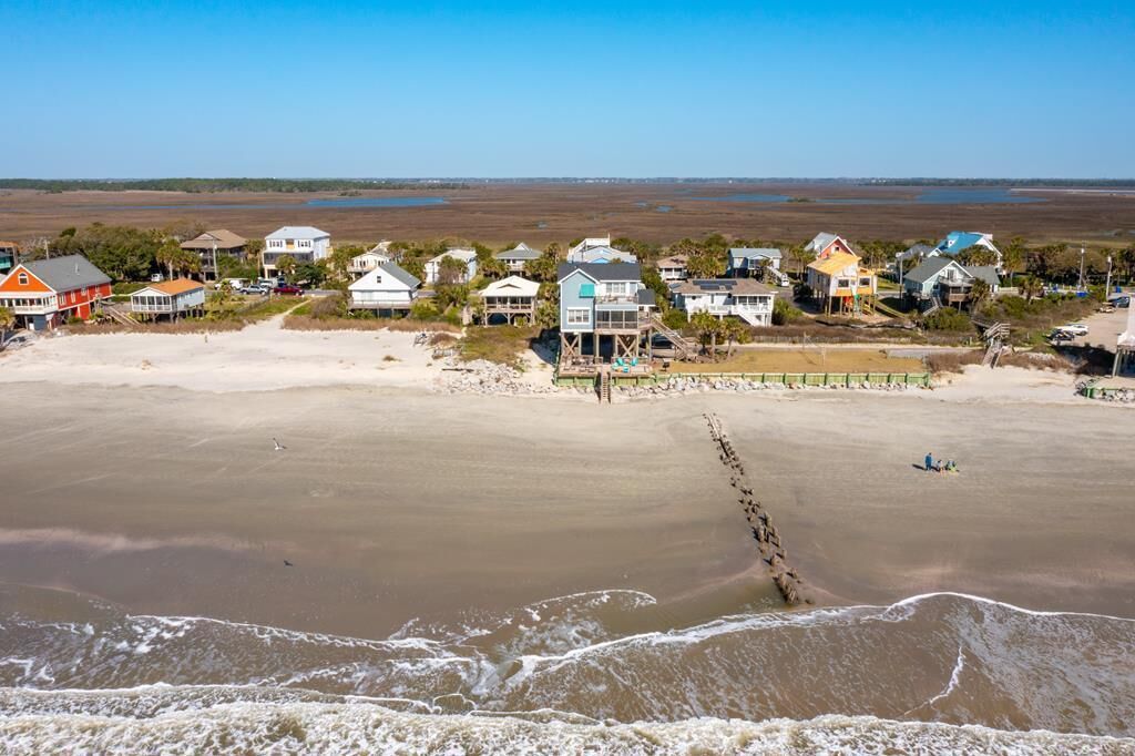 A coastal residential area with houses along the beach, a pier, and a view of the ocean.