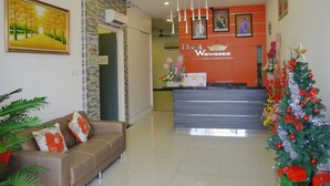 A hotel reception area with a modern design, featuring a reception desk, a sofa with decorative pillows, a Christmas tree, and framed artwork on the walls. - Hotel Wawasan (Simpang Renggam)