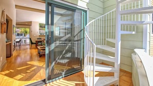 Ein geräumiger Raum mit einer großen Schiebeglaswand, die zu einem Außenbereich führt, einer weißen Wendeltreppe und einem Essbereich mit Tisch und Stühlen.