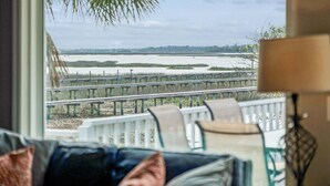 A view through a window with a railing, a body of water, and a distant shoreline. - Ocean, Marsh, & River Views! Dock For Fishing & Sunsets (Folly Beach)
