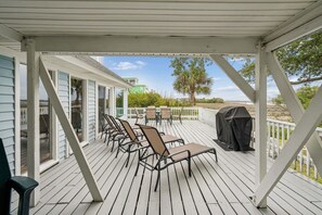 A covered outdoor deck with chairs and a grill, overlooking a residential area.