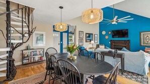 A modern living room with a dining table, chairs, a staircase, and a blue accent wall. - Ocean, Marsh, & River Views! Dock For Fishing & Sunsets (Folly Beach)