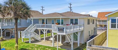 A beachfront property with a covered deck, a swing, and a sign indicating it's a vacation rental.