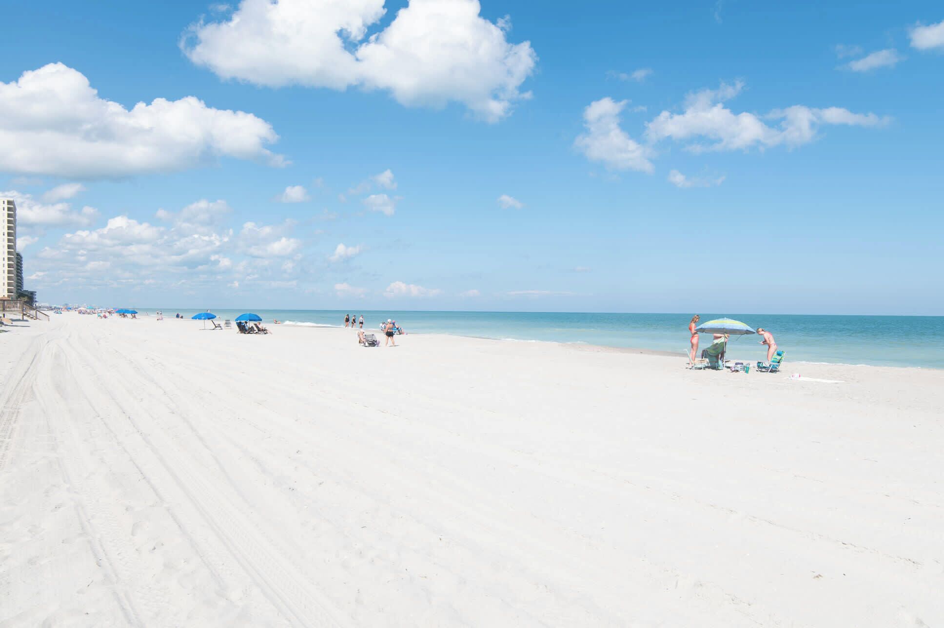 A beach with a clear sky, a few people, and a building in the background.