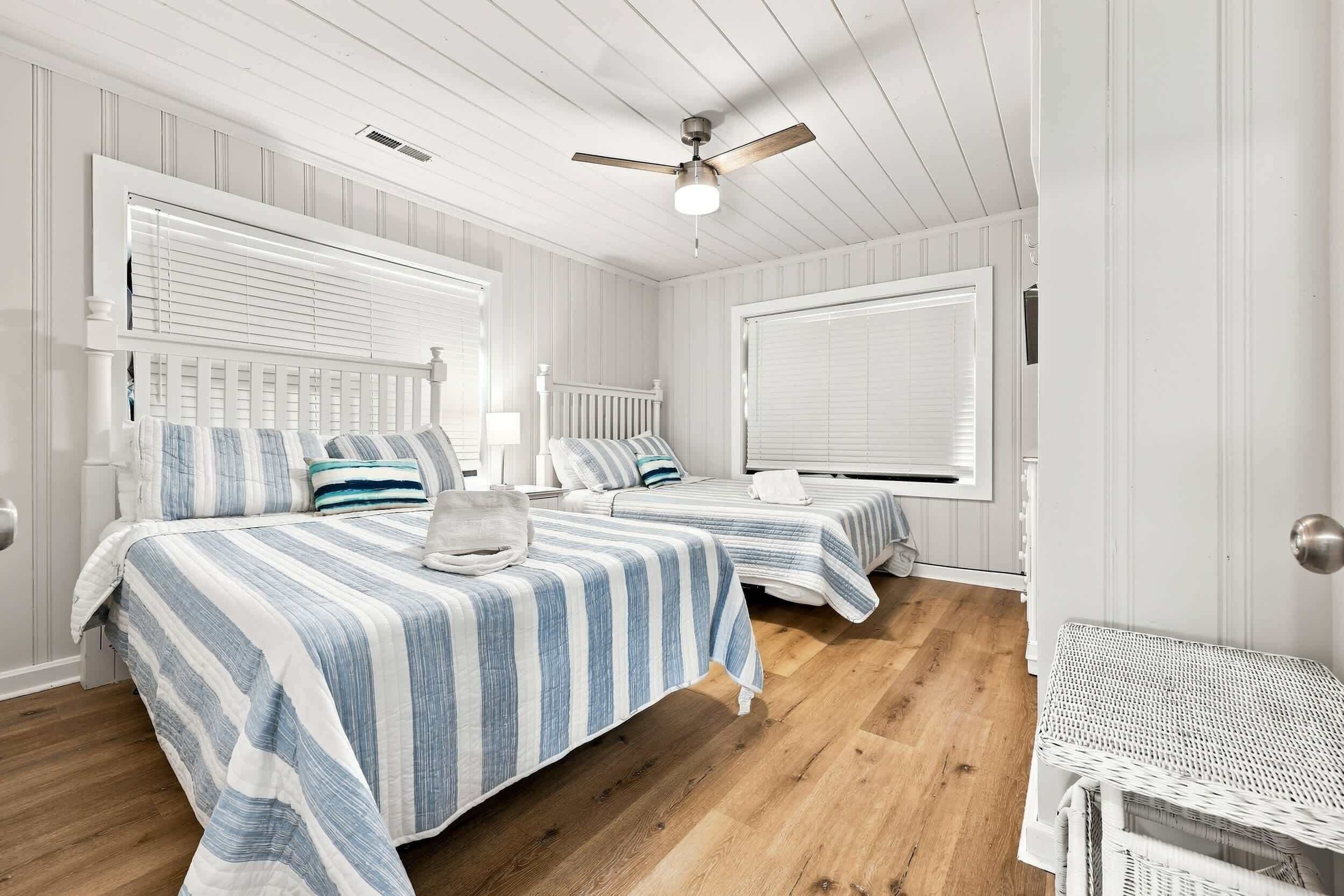 A room with two beds, a ceiling fan, and a window with blinds.