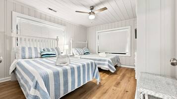 A room with two beds, a ceiling fan, and a window with blinds.