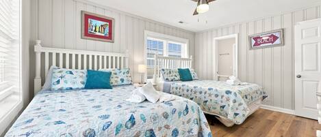 A hotel room with two beds, a ceiling fan, a window with blinds, and a door with a sign.