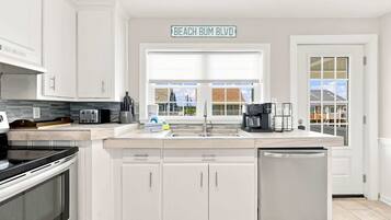 A modern kitchen with white cabinetry, a built-in oven, a dishwasher, and a coffee maker.