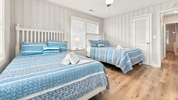 Ein Schlafzimmer mit zwei Betten, weißen Wandverkleidungen und einem Deckenventilator.