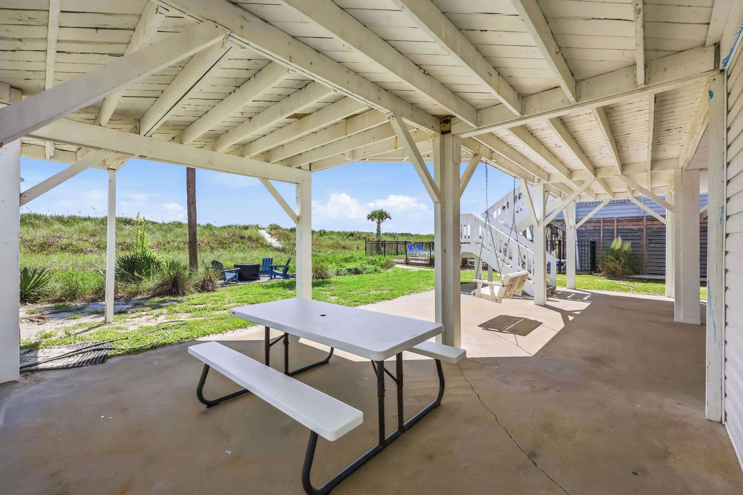Un espacio al aire libre cubierto con una mesa de picnic, un conjunto de columpios y vistas del paisaje circundante.