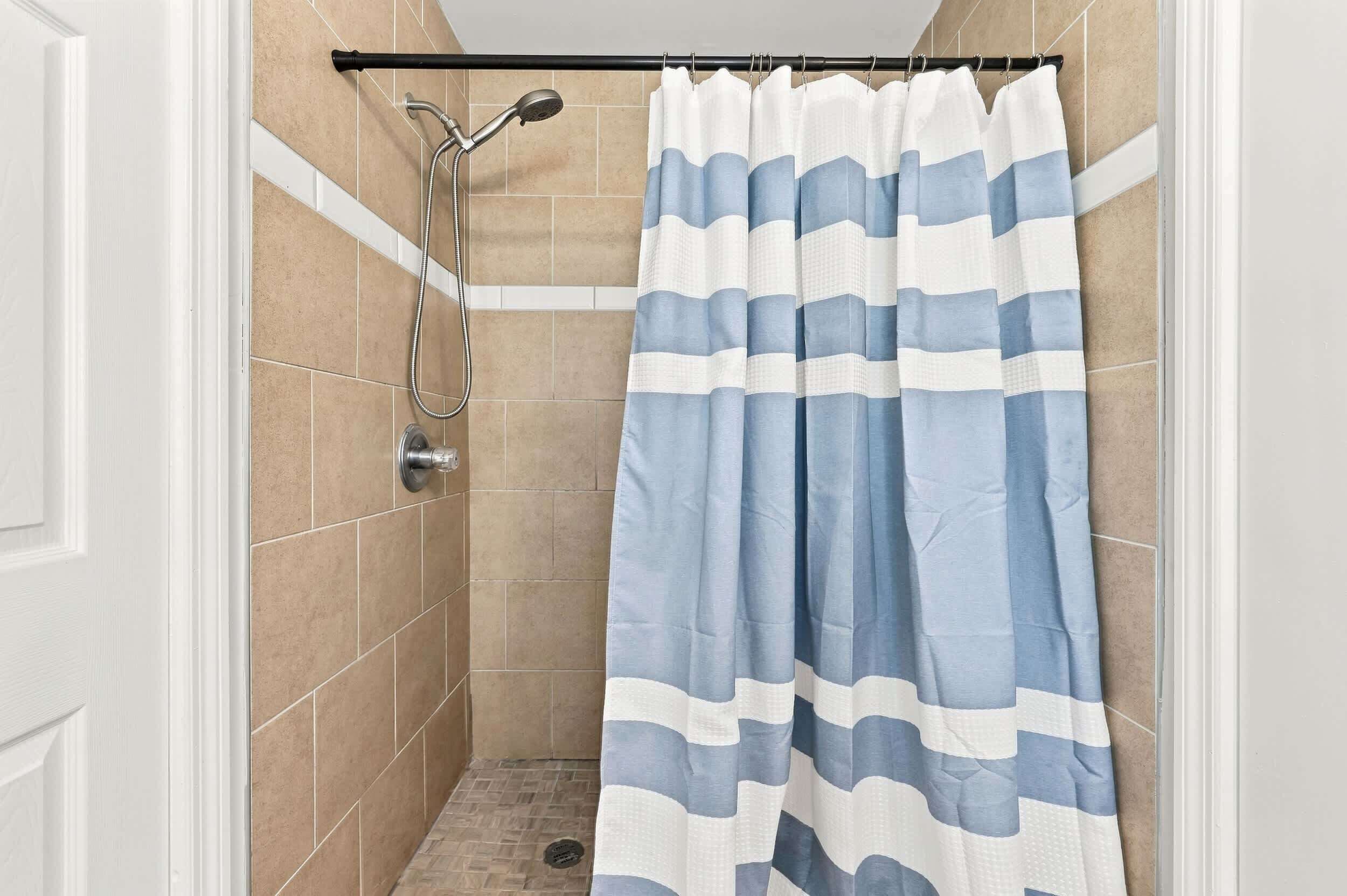 Eine Dusche mit gestreiftem Duschvorhang, einer Handbrause und einem am Wand montierten Wasserhahn.