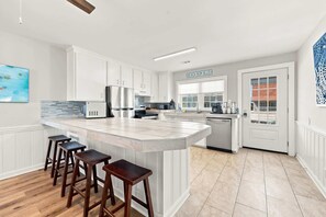 Una cocina moderna con armarios blancos, una isla de mármol con taburetes y vistas a la calle.