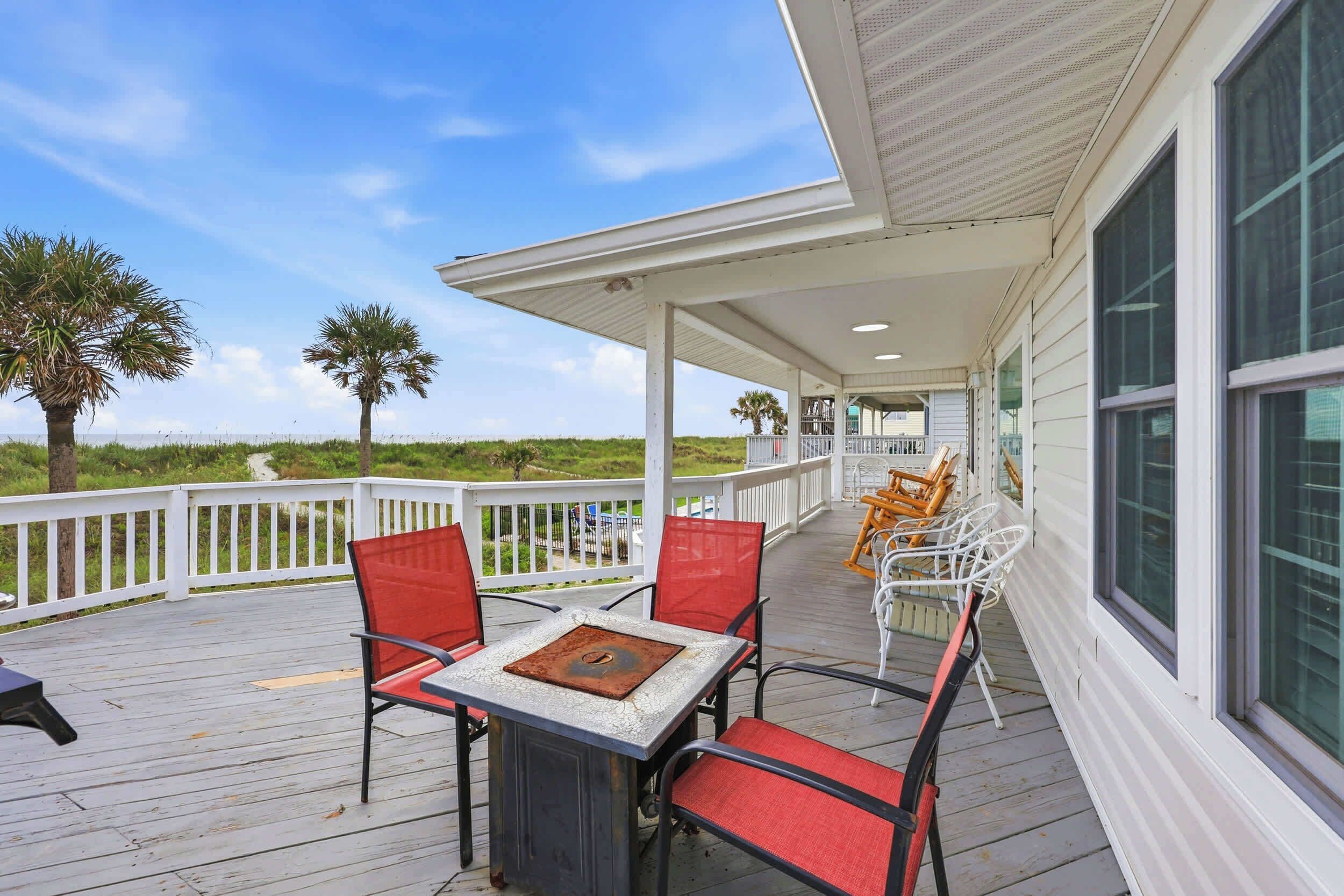 A covered outdoor area with a table and chairs, a railing, and a view of the beach.