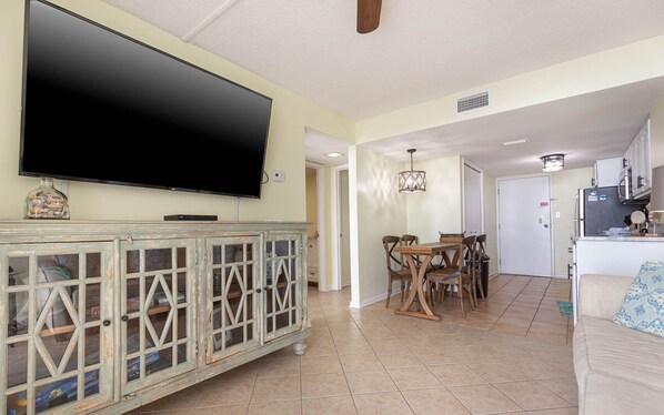 Una sala de estar con televisor, una mesa de comedor con sillas, una zona de cocina y un sofá.