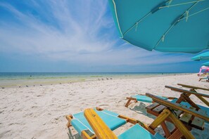 Ein Strand mit blauem Himmel, sandigem Ufer und Holzliegen.