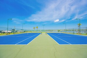 Ein Tennisplatz mit Netz in der Mitte, umgeben von einem Zaun, mit blauem Himmel darüber.