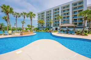 Un hotel con piscina, palmeras y un edificio con varios balcones.