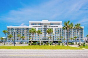 A multi-story hotel with balconies, a parking area, and palm trees.