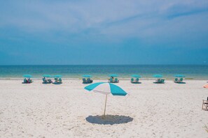 Ein Strand mit mehreren türkisblauen Sonnenschirmen und Liegestühlen.
