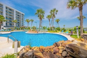 A swimming pool with lounge chairs and palm trees, surrounded by a hotel building.