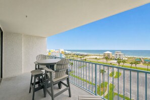 Ein Balkon mit Blick auf Strand und Meer, ausgestattet mit einem Tisch und Stühlen.