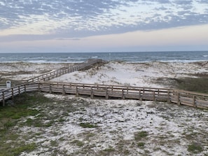 A wooden boardwalk leading to a sandy beach area with a view of the ocean.