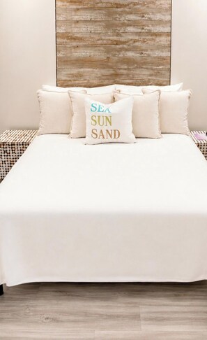A bed with a white bedspread and multiple pillows, one with the text 'SEA SUN SAND'.