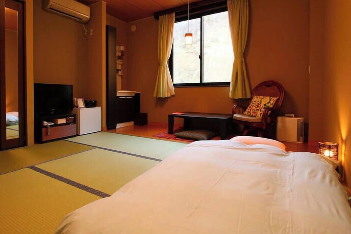 A traditional Japanese room with tatami flooring, a bed, a TV, a desk, and a chair.
