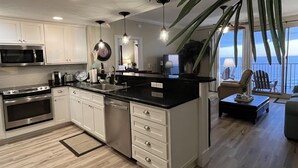 A modern kitchen with white cabinets, stainless steel appliances, and a black countertop. There is a large window with a view of the ocean. - Updated Butler's Treasure Island,new master bath! Beach Service for 2 Included! (Panama  City  Beach)