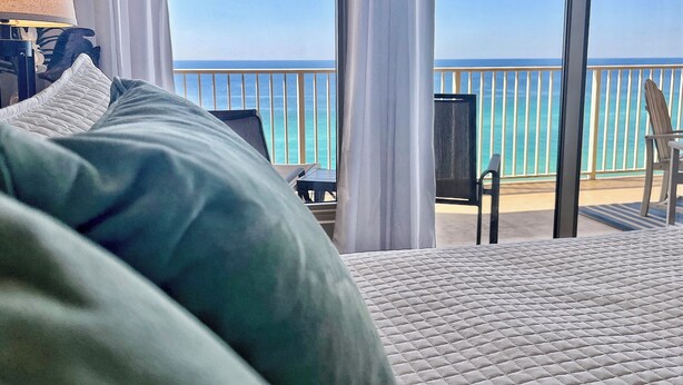 A hotel room with a bed, a chair, and a view of the ocean through large windows. - Updated Butler's Treasure Island,new master bath! Beach Service for 2 Included! (Panama  City  Beach)